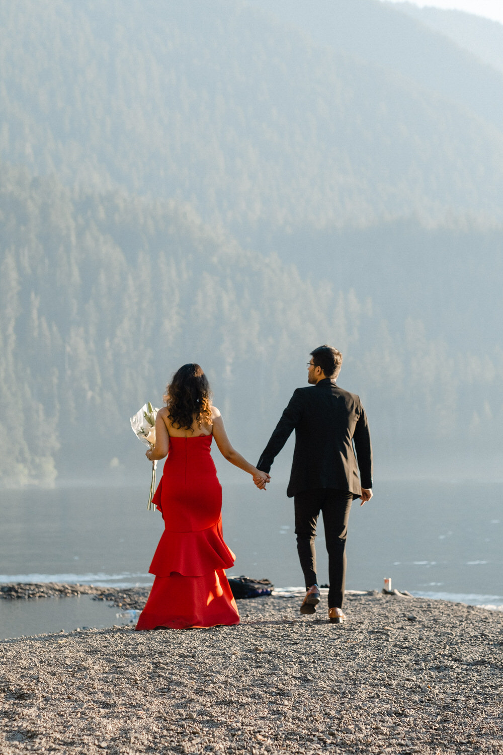Bride and groom hold hands and walk along the beach of Lake Crescent in Olympic National Park