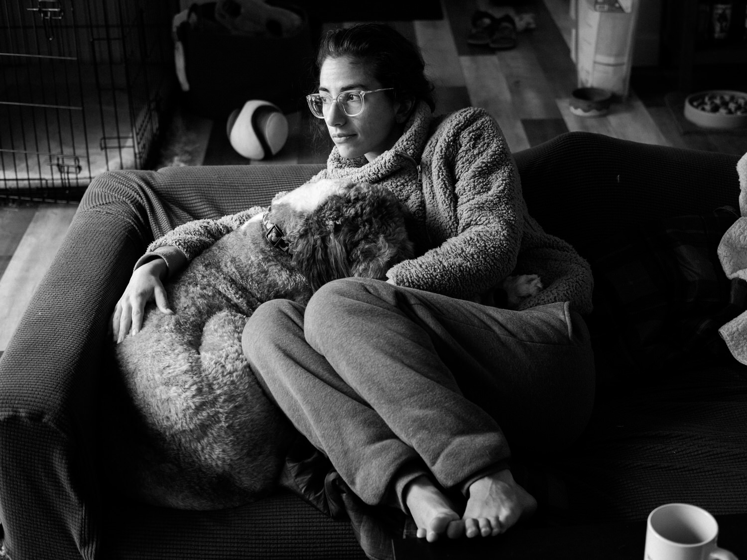 Black and white photo of a woman curled up on a coach snuggling her dog
