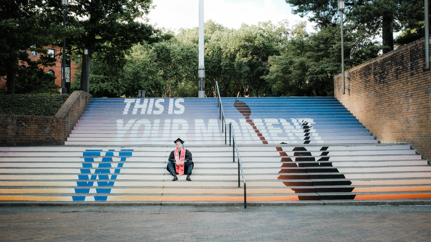 University of Washington Graduate sits on steps in his cap and gown