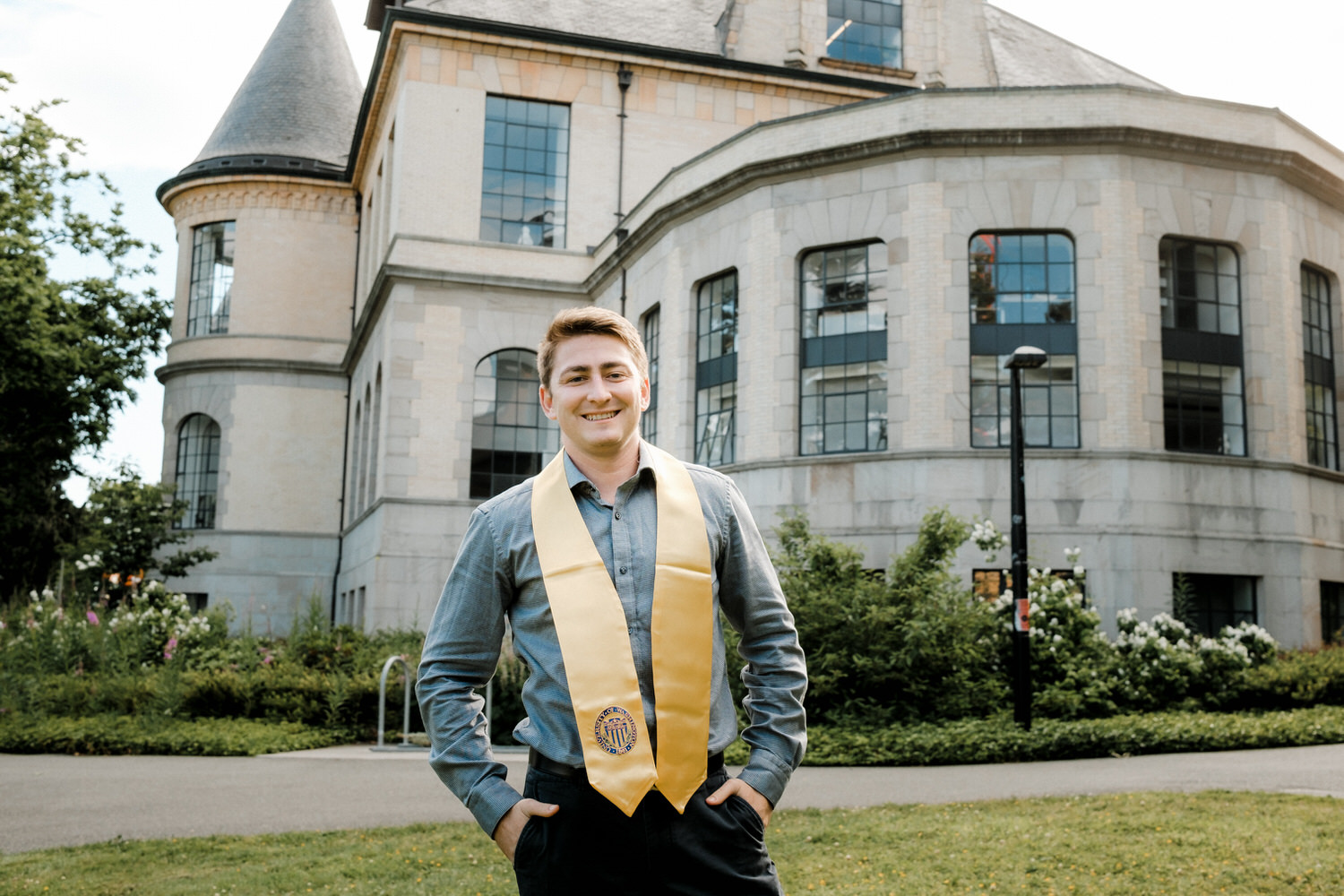 UW graduate posing in front of business school with is yellow sash on