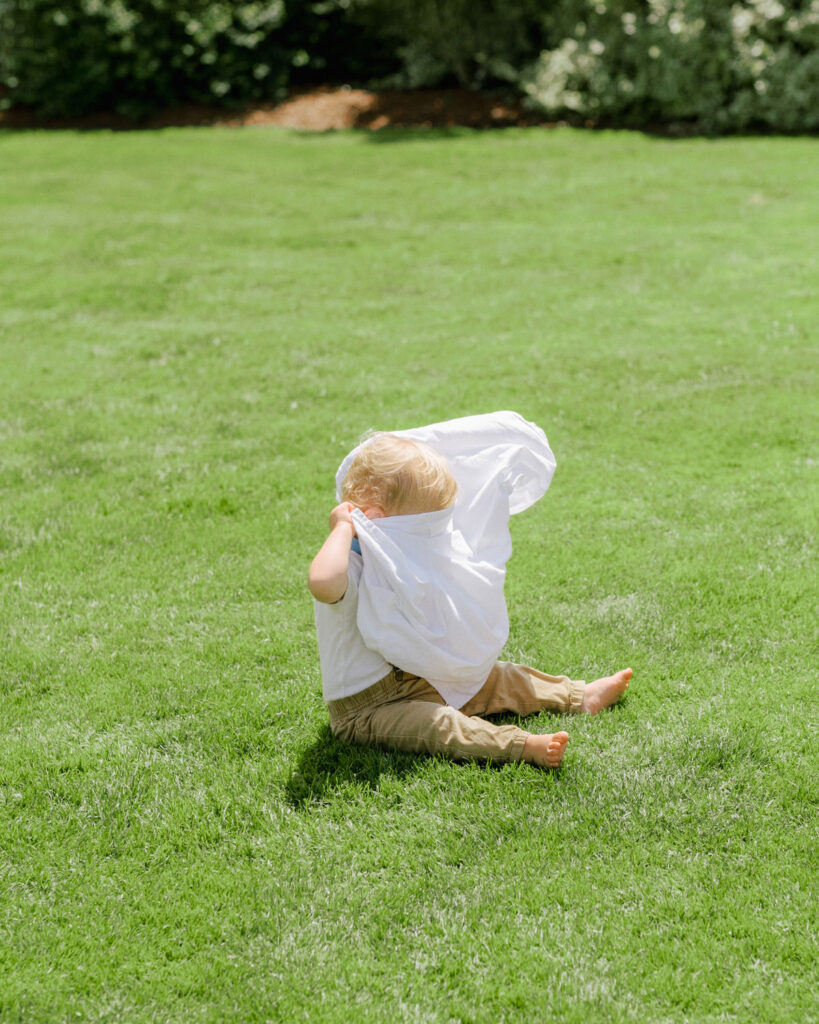 a child sitting on grass with a white sheet covering his face