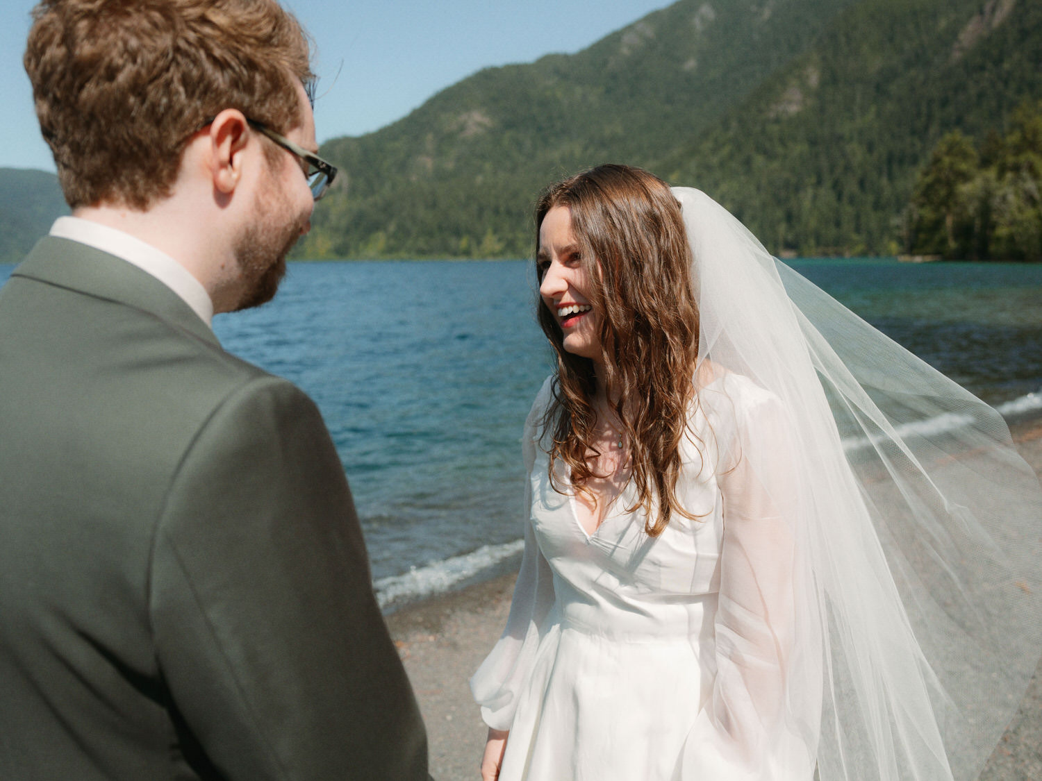 Bride laughing with groom on lakeshore during outdoor Olympic National Park wedding