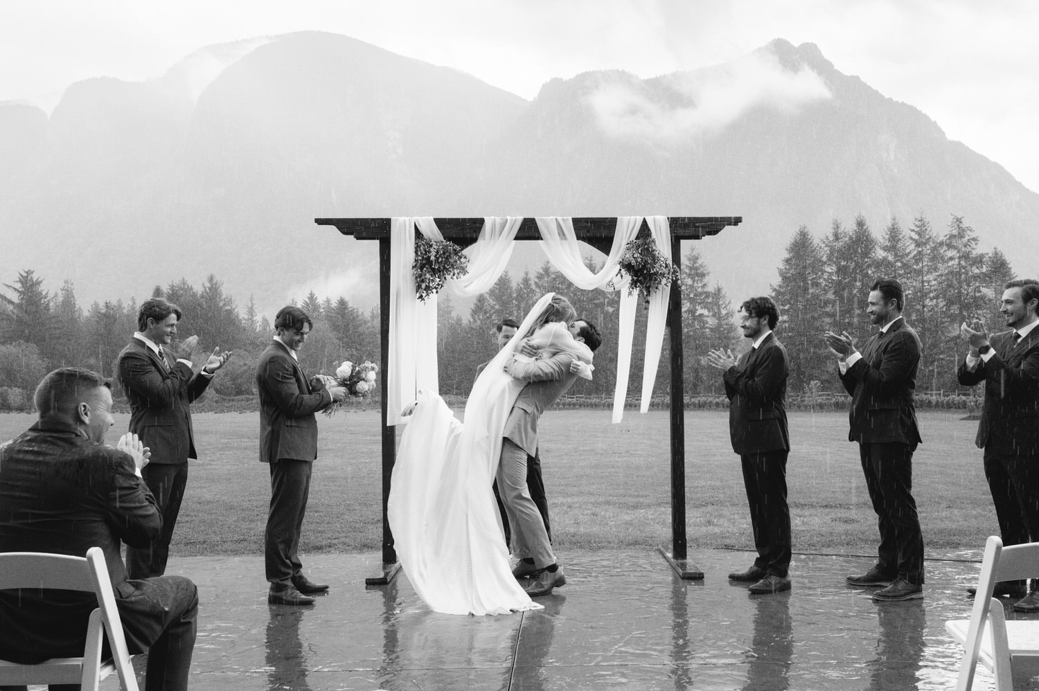 The Best Documentary Wedding Photography of 2025 4 A couple embraces under a simple wooden arch as rain falls during a mountain wedding