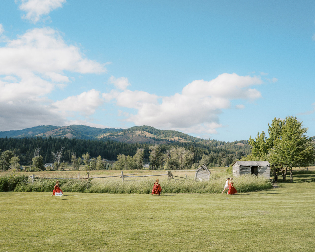 Flower girls in red dresses walk in a line at the cattle barn wedding.