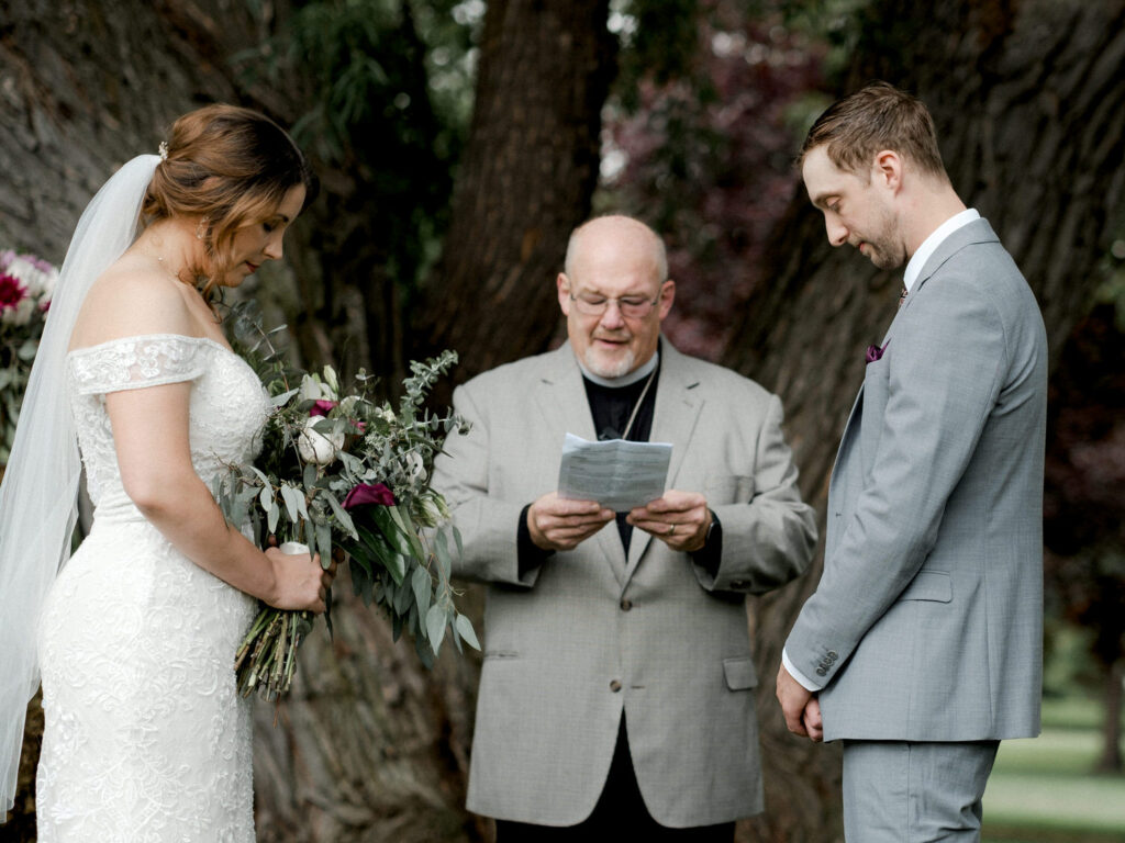 Bride and groom bow their head as the officiant reads a prayer