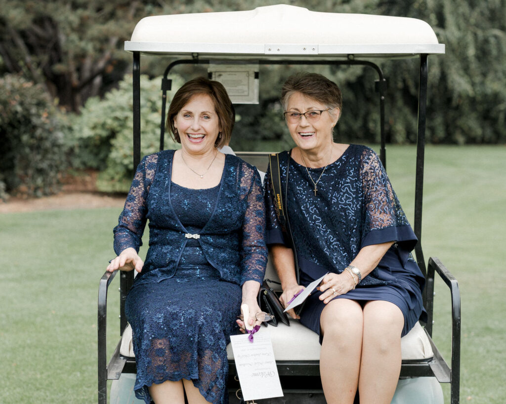Mother of the bride and the mother of the groom ride off on a golf cart