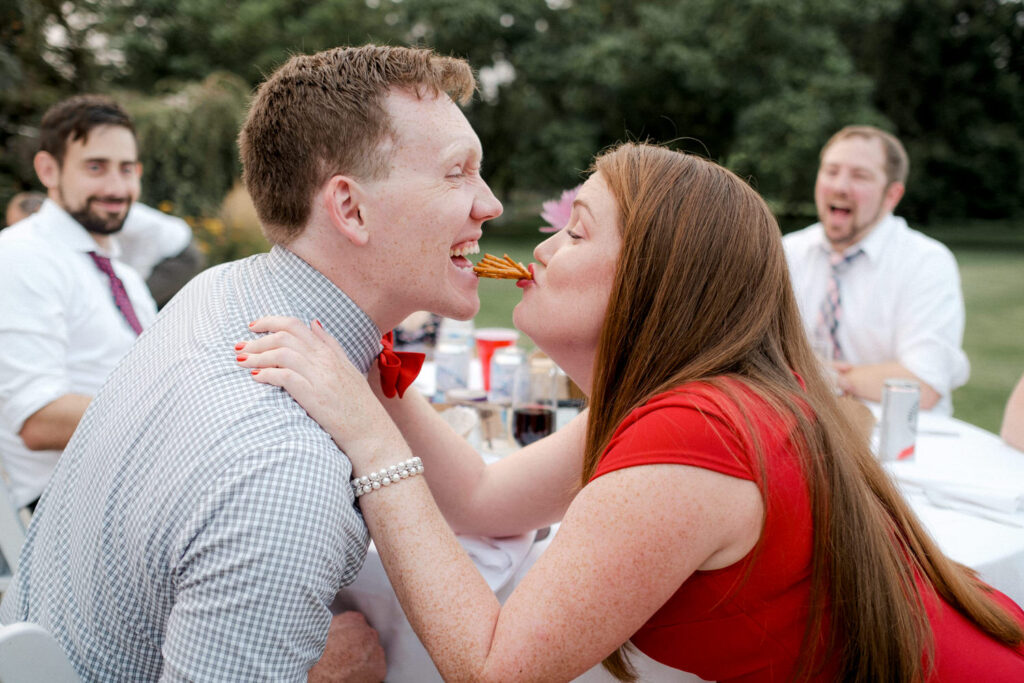 Two wedding guests try to kiss with pretzels in their mouth