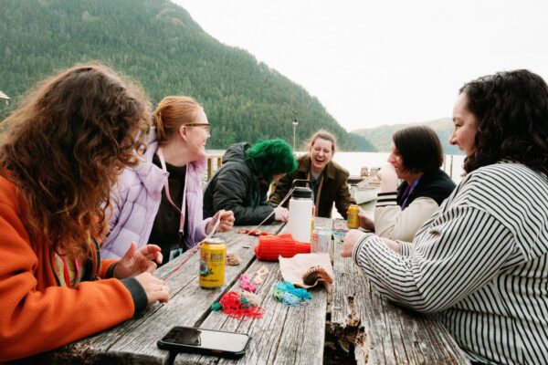 Olympic National Park Wedding | Sara and Robert's Summer Camp Wedding Weekend at NatureBridge 6 Group of friends laughing around picnic table with drinks during welcome dinner at NatureBridge Olympic