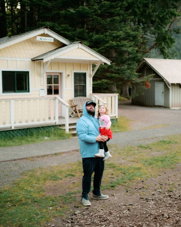 Olympic National Park Wedding | Sara and Robert's Summer Camp Wedding Weekend at NatureBridge 5 Parent holding child outside cabin during welcome dinner at NatureBridge Olympic summer camp wedding