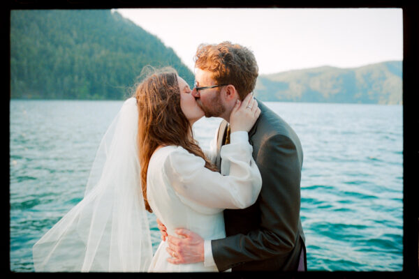 Olympic National Park Wedding | Sara and Robert's Summer Camp Wedding Weekend at NatureBridge 40 Bride and groom kissing by the lake at sunset during outdoor summer camp wedding