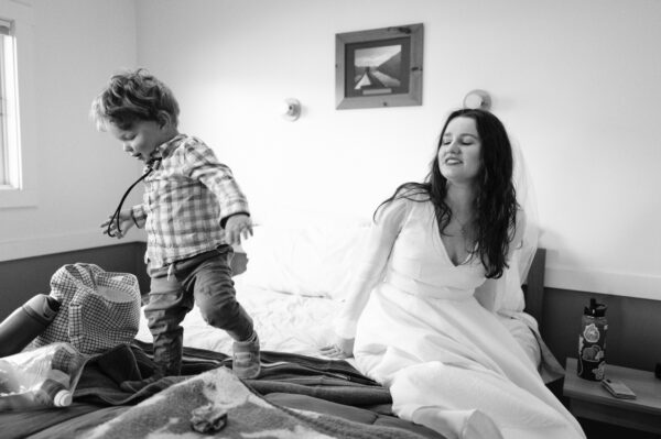 Olympic National Park Wedding | Sara and Robert's Summer Camp Wedding Weekend at NatureBridge 30 Bride sitting on bed with child during getting ready at intimate summer camp wedding