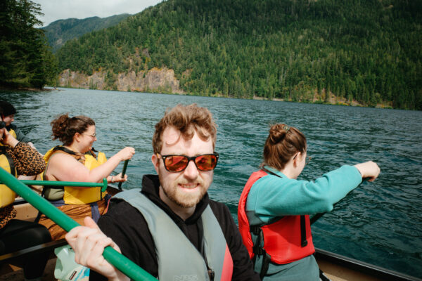 Olympic National Park Wedding | Sara and Robert's Summer Camp Wedding Weekend at NatureBridge 55 Groom paddling canoe with wedding guests on Lake Crescent during summer camp wedding weekend