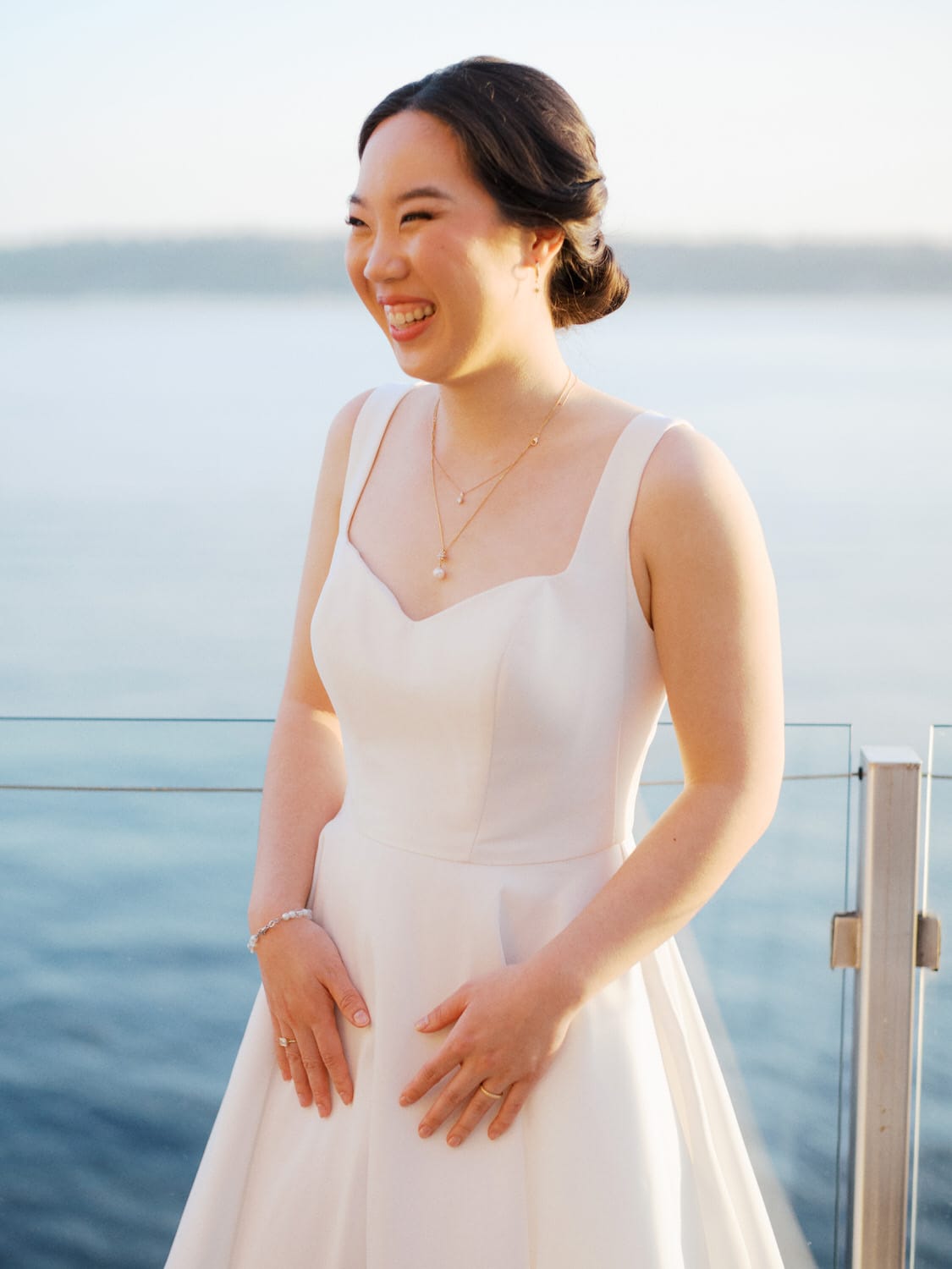 The Edgewater Hotel Wedding | Candid Seattle Wedding Photography for Amy & Mike 23 Bride standing by the waterfront at the Edgewater Hotel in Seattle, her wedding dress catching soft sunset light
