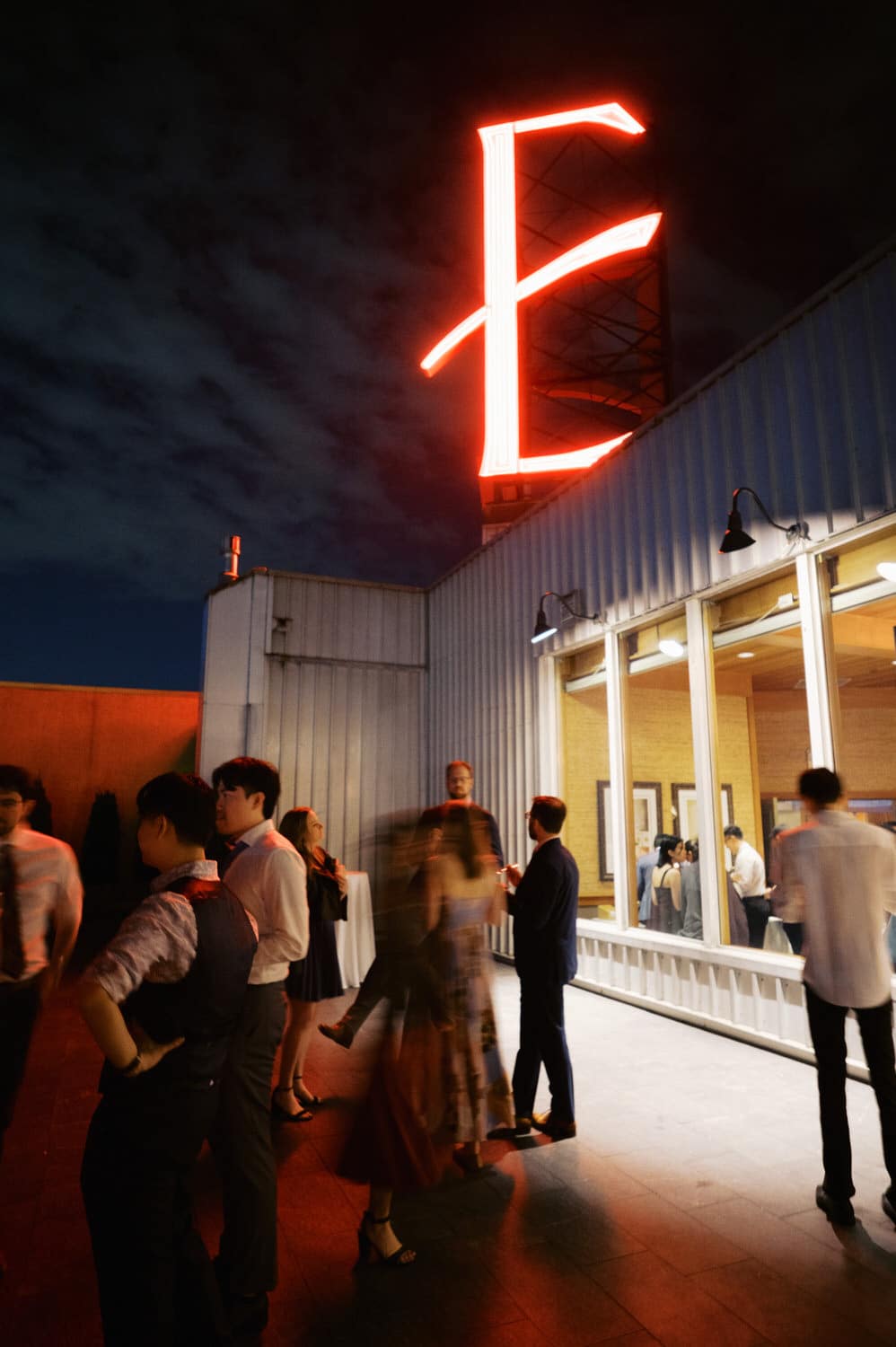 The Edgewater Hotel Wedding | Candid Seattle Wedding Photography for Amy & Mike 35 Guests talking outside under the glowing red Edgewater Hotel sign at night in Seattle.